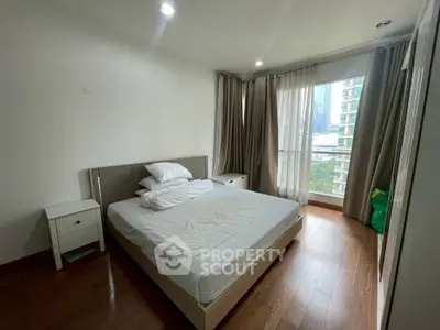 Spacious bedroom with large window and wooden flooring in modern apartment