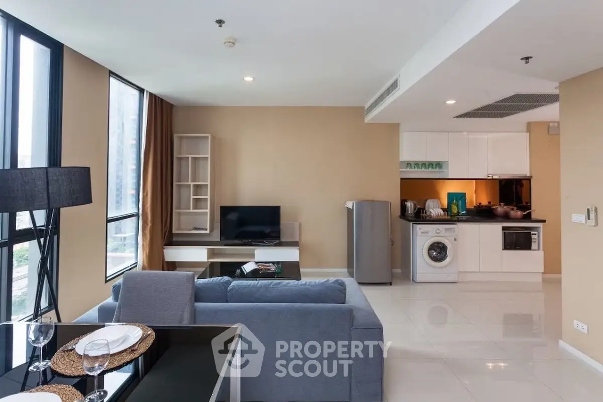 Modern living room with open kitchen, featuring a washing machine and sleek appliances.