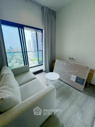 Modern living room with city view and large window, featuring a cozy sofa and new TV.