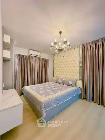 Luxurious bedroom with elegant chandelier and plush headboard in modern apartment.