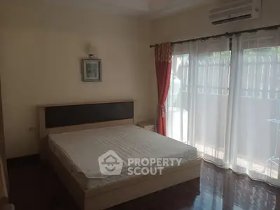 Spacious bedroom with large window and balcony access, featuring a modern bed and elegant curtains.