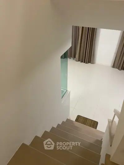 Modern staircase leading to a bright living space with elegant curtains and tiled flooring.