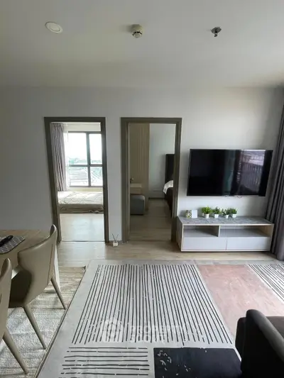 Modern living room with stylish decor and wall-mounted TV, open to bedroom view.