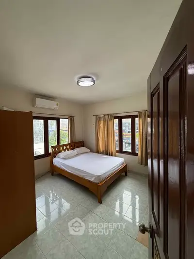 Spacious bedroom with large windows and natural light, featuring a comfortable bed and air conditioning.