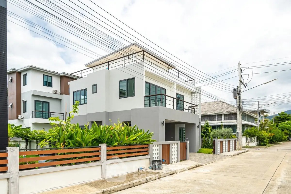 Modern two-story house with rooftop terrace and lush greenery in suburban neighborhood.