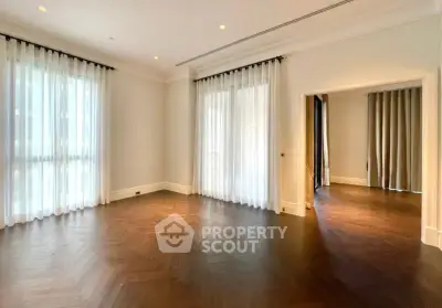 Spacious living room with elegant hardwood floors and large windows with sheer curtains.