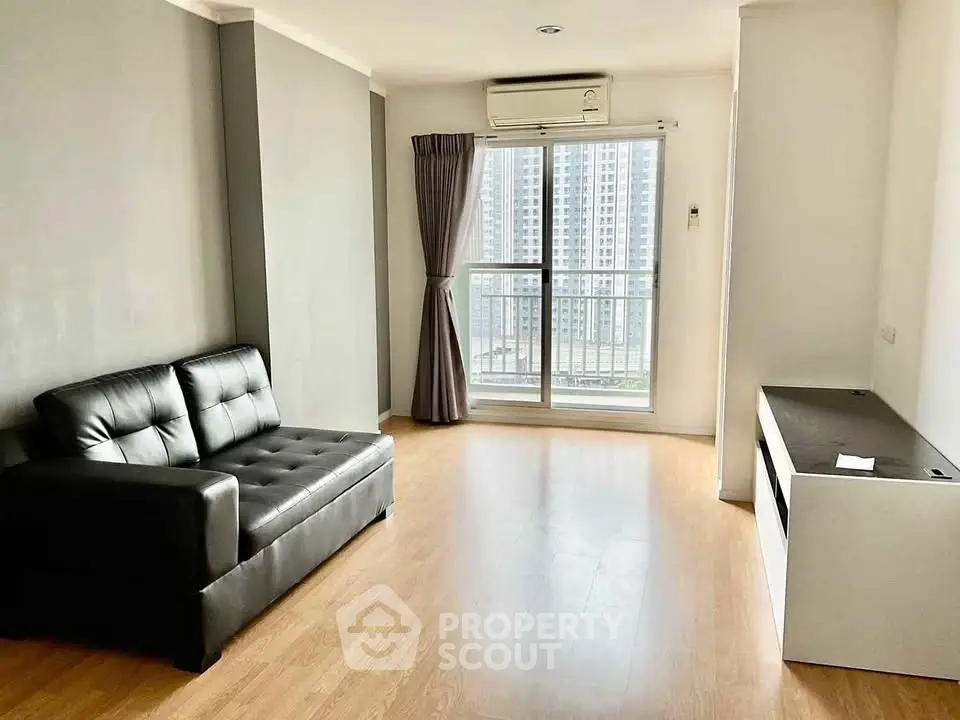 Modern living room with sleek black sofa and large window offering city view.