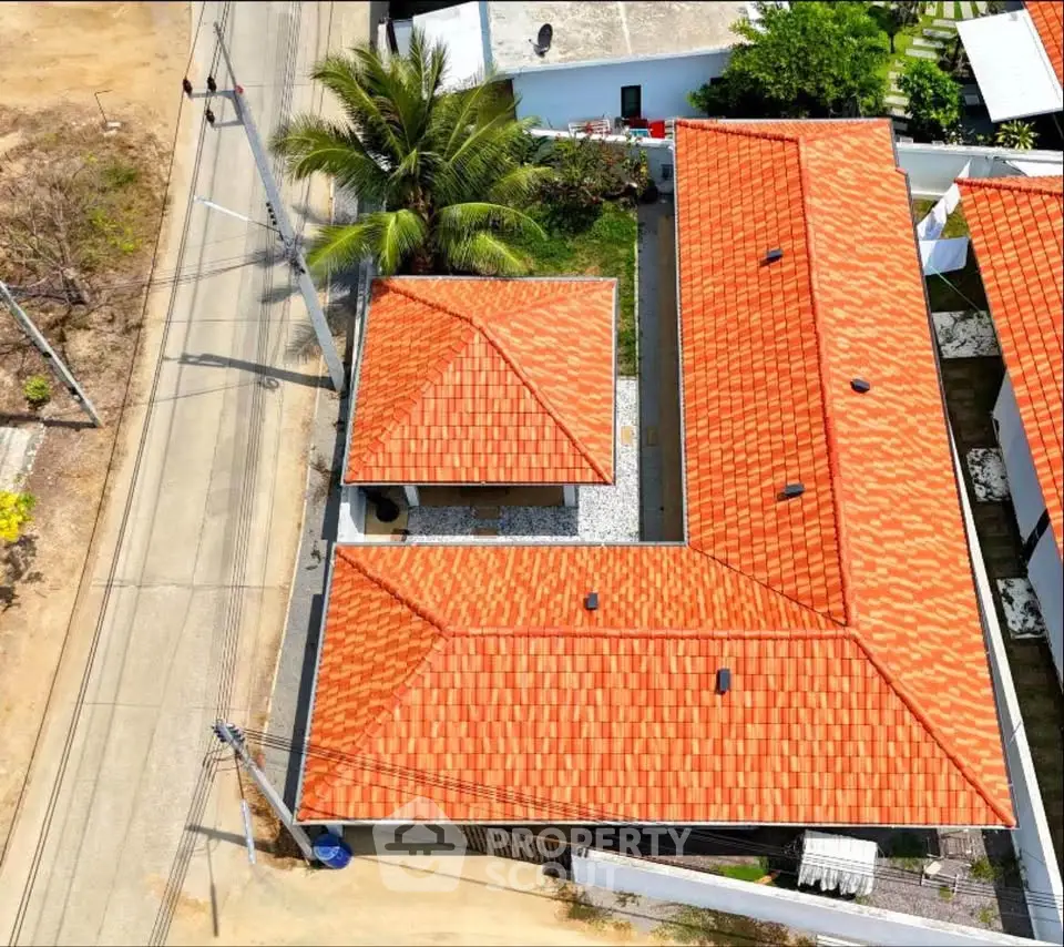 Aerial view of a property with vibrant red-tiled roofs and lush greenery, showcasing a spacious layout.