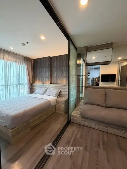 Modern bedroom with glass partition and cozy seating area, featuring stylish decor and natural light.