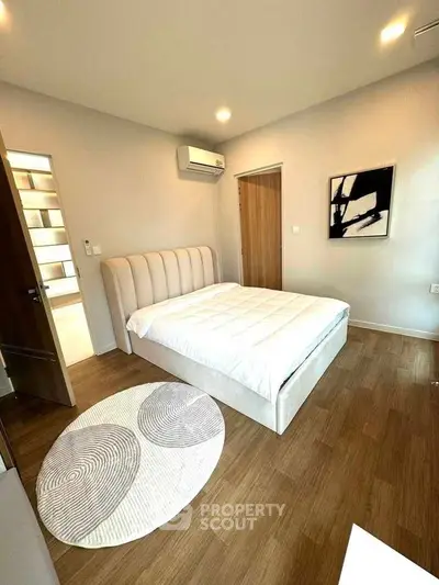 Modern bedroom with stylish decor and wooden flooring, featuring a cozy bed and contemporary artwork.
