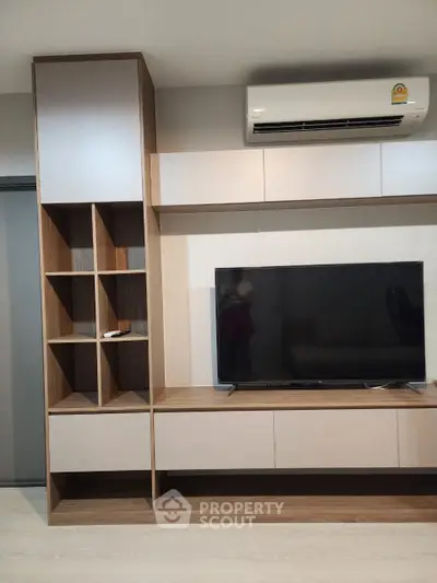 Modern living room with custom-built wooden entertainment unit featuring ample shelving and a large flat-screen TV, complemented by a sleek air conditioning unit above.