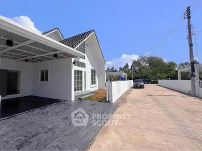 Modern white house with spacious driveway and carport, surrounded by lush greenery under a clear blue sky.