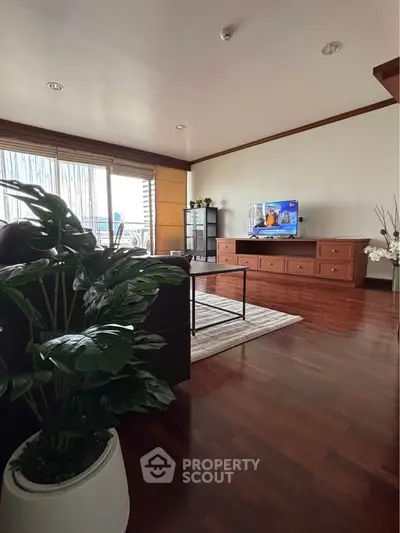 Spacious living room with modern decor and large TV, featuring wooden flooring and natural light.