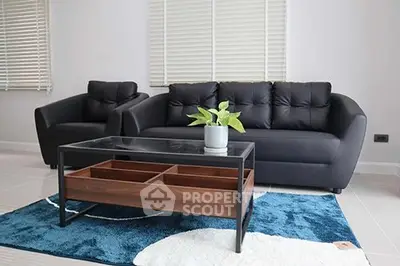 Modern living room with sleek black sofa, armchair, and stylish glass coffee table on a plush blue rug.