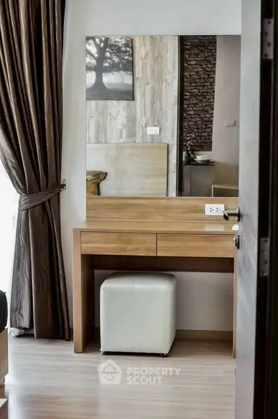 Stylish bedroom with elegant wooden vanity and plush stool, featuring floor-to-ceiling curtains and modern decor.