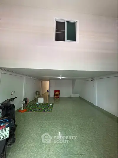 Spacious tiled garage with scooter and storage space, featuring a small window and minimal decor.