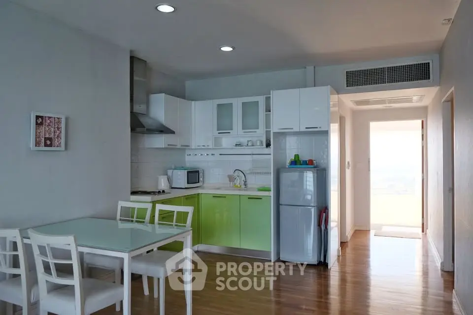 Modern kitchen with green cabinets, dining area, and natural light in a stylish apartment.