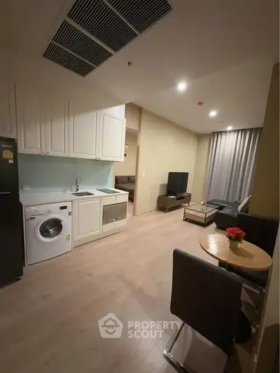 Modern open-plan living room with kitchen, featuring washing machine and cozy dining area.