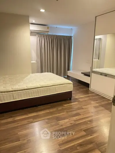 Spacious bedroom with wooden flooring and modern furnishings in a stylish apartment.