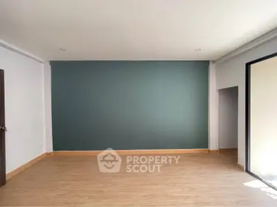 Spacious empty room with wooden flooring and large window, ideal for customization.