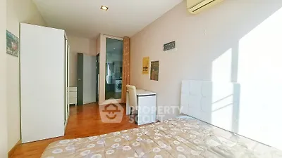 Bright bedroom with modern decor and wooden flooring, featuring a washing machine in the background.