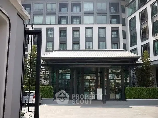 Modern apartment building entrance with sleek glass facade and lush greenery.