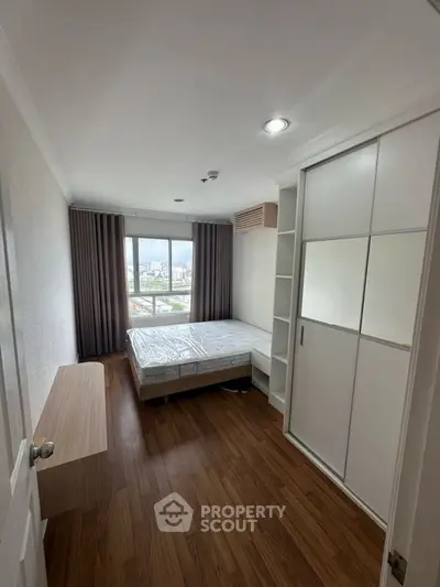 Modern bedroom with wooden flooring and large window offering city views.