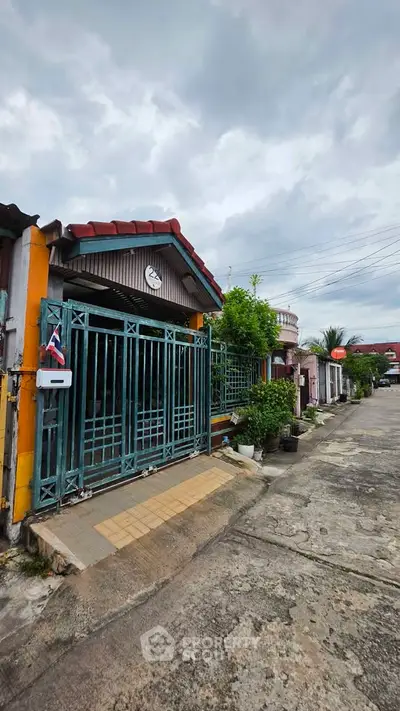 Charming residential street view with gated entrance and lush greenery, perfect for serene living.