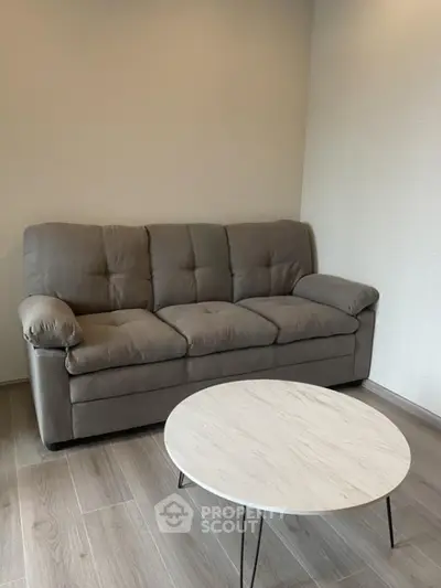 Modern living room with a stylish gray sofa and round marble coffee table on wooden flooring.