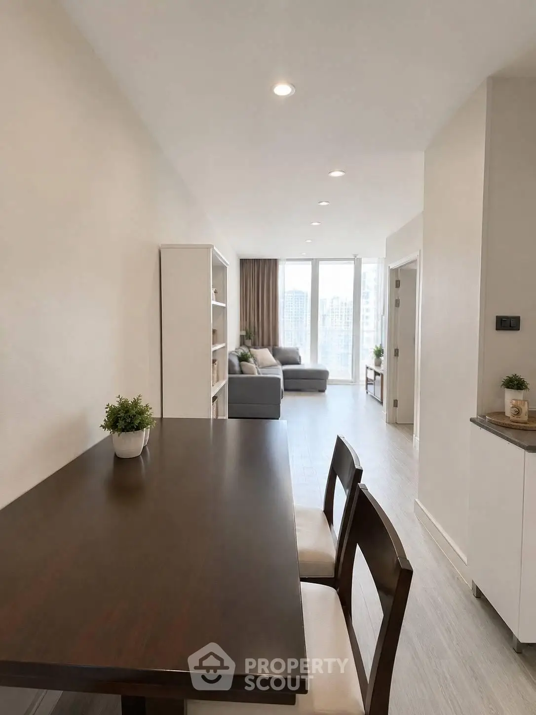 Modern open-plan living room with dining area and city view, featuring sleek furniture and natural light.