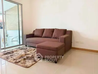Cozy living room with modern brown sofa and plush rug, adjacent to a bright balcony.