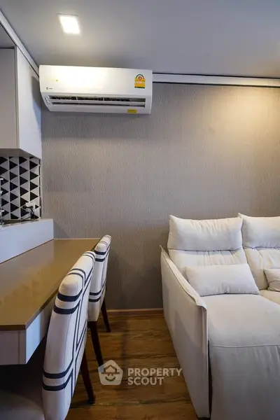 Modern living room with stylish furniture and air conditioning, featuring a cozy sofa and elegant dining chairs.