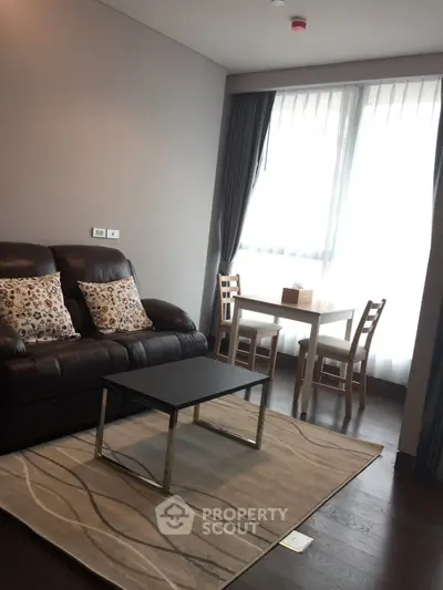Modern living room with leather sofa, stylish rug, and dining area by large window.
