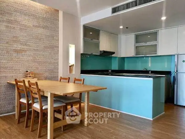 Modern kitchen with open layout and dining area, featuring sleek cabinetry and wooden flooring.