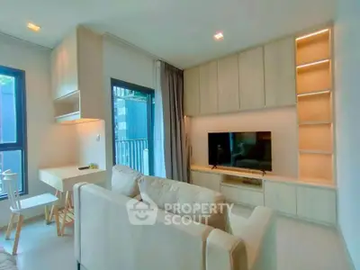 Modern living room with built-in shelves and large TV, featuring natural light and cozy seating.