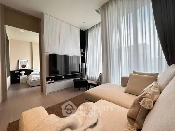 Modern living room with cozy sofa and large TV, leading to a stylish bedroom.