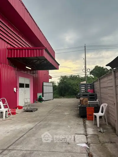 Industrial warehouse exterior with vibrant red facade and spacious concrete driveway.