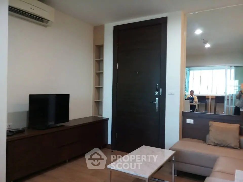 Modern living room with sleek furniture and large wooden door, featuring a cozy sofa and flat-screen TV.