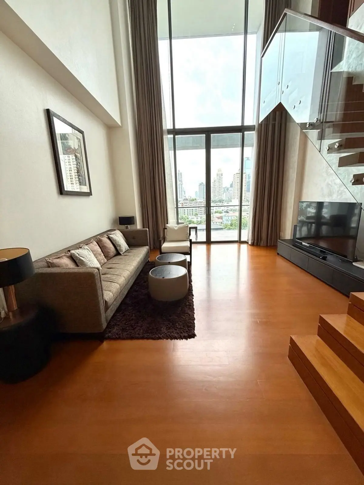 Spacious modern living room with high ceiling and city view, featuring elegant furniture and wooden flooring.