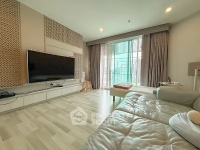 Spacious modern living room with large TV and balcony access, featuring stylish decor and ample natural light.
