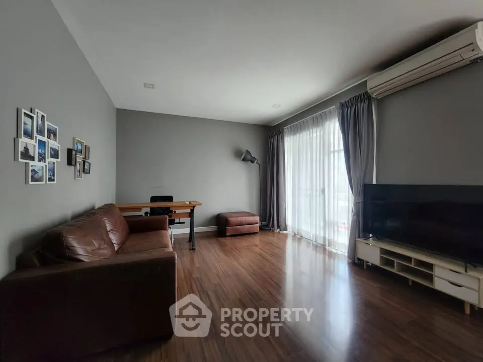 Spacious living room with modern decor, large window, and wooden flooring, perfect for relaxation and entertainment.