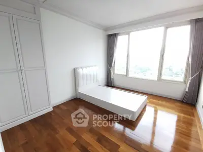 Spacious bedroom with large window and wooden flooring in modern apartment