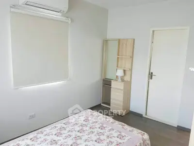 Cozy bedroom with floral bedding and minimalist decor, featuring air conditioning and natural light.