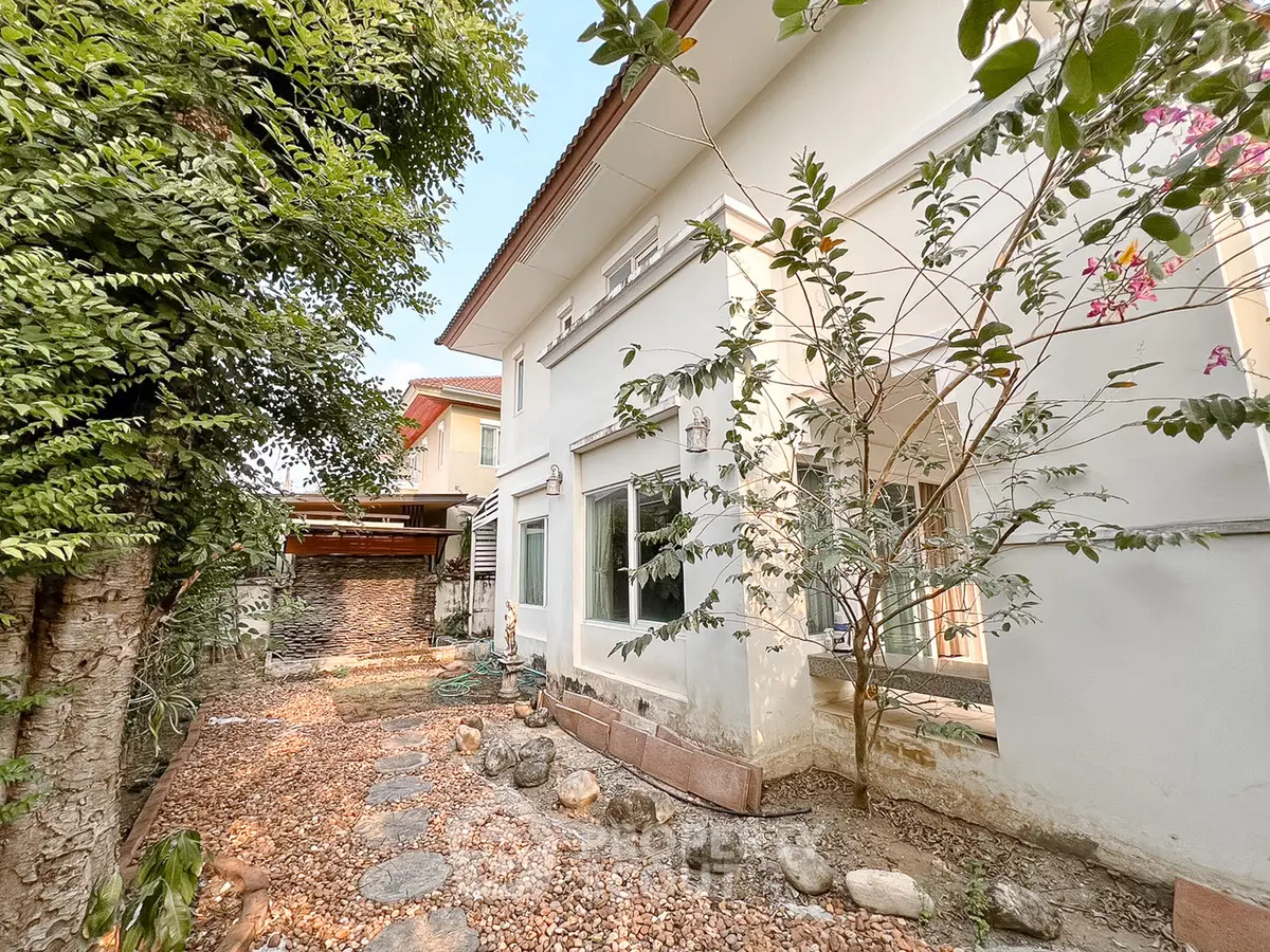 Charming white house with lush garden and stone pathway, perfect for serene living.