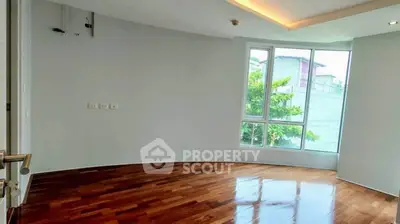 Spacious empty room with wooden flooring and large window offering natural light.