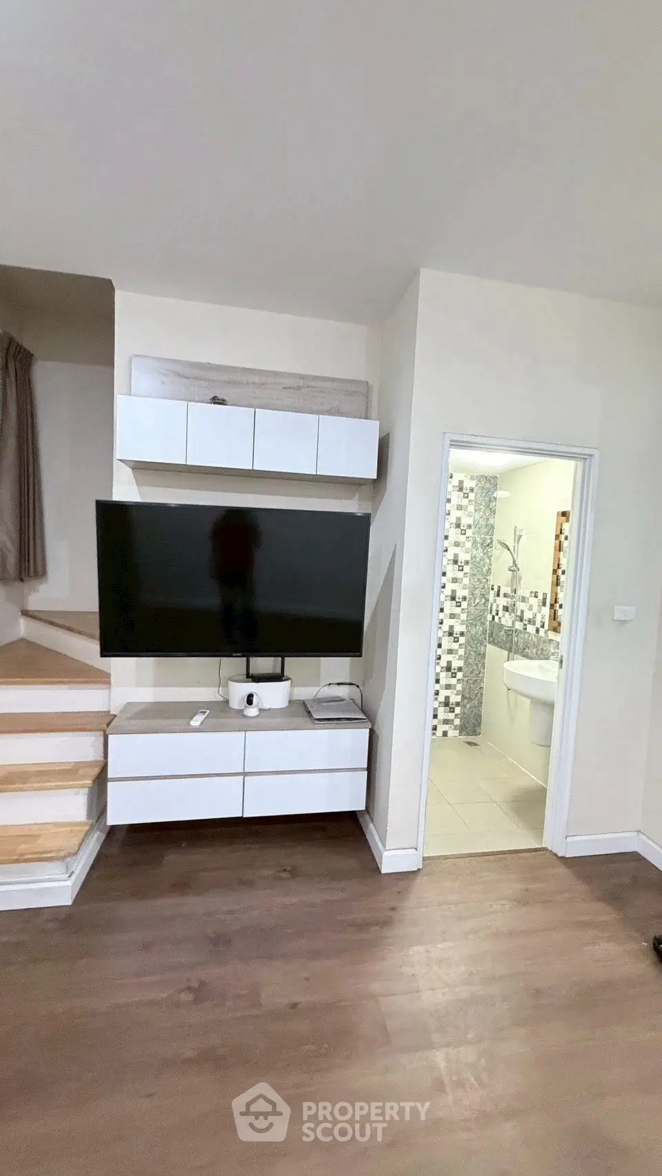 Modern living room with sleek TV setup and adjacent bathroom entry, featuring stylish wooden flooring.