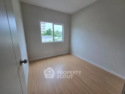 Spacious empty bedroom with wooden flooring and large window view.