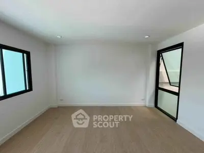 Spacious empty room with wooden flooring and large windows, perfect for customization.