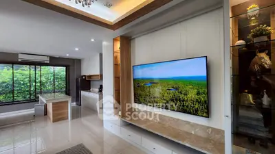 Modern living room with open kitchen, large TV, and natural light from big windows.