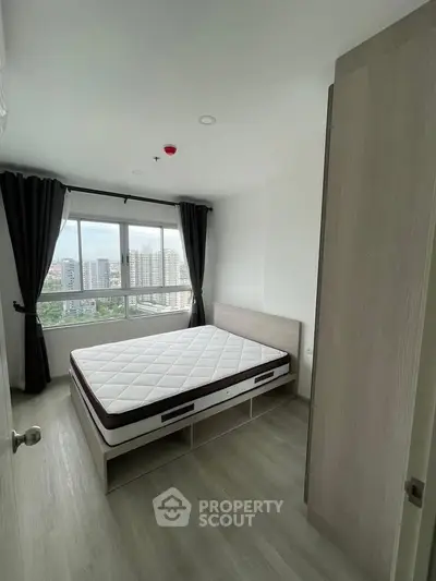 Modern bedroom with large window offering city views, featuring a minimalist design and ample natural light.